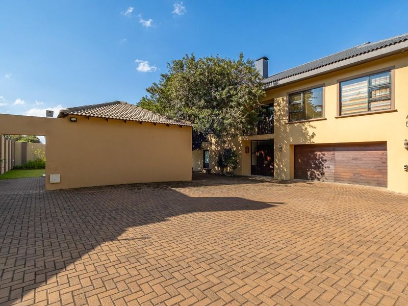 Spacious front exterior view featuring a large paved driveway, a double-story building facade with a wooden garage door, and a perimeter wall.