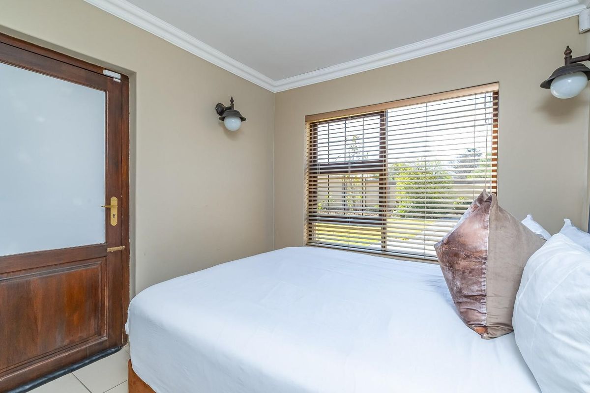 A well-maintained bedroom featuring a timber door with frosted glass, venetian blinds, and wall-mounted lighting fixtures.