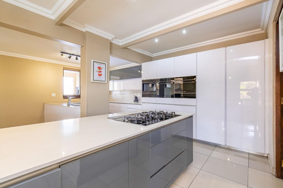Modern kitchen featuring high-gloss cabinetry, stone countertops, a central island with a gas hob, and integrated built-in ovens.