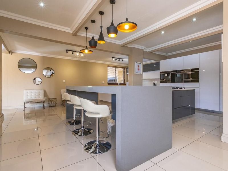 Modern open-plan living area featuring a sleek kitchen island, integrated appliances, built-in fireplace, and polished tiled flooring with contemporary lighting.