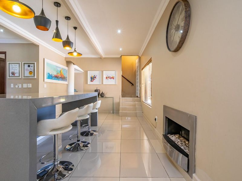 Modern open-plan living area featuring a sleek kitchen island, built-in fireplace, tiled flooring, and contemporary pendant lighting leading to an internal staircase.