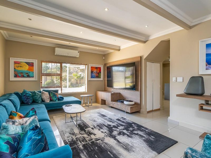 A well-maintained living room featuring tiled floors, recessed ceiling lighting, crown molding, and a custom built-in media console with integrated air conditioning.
