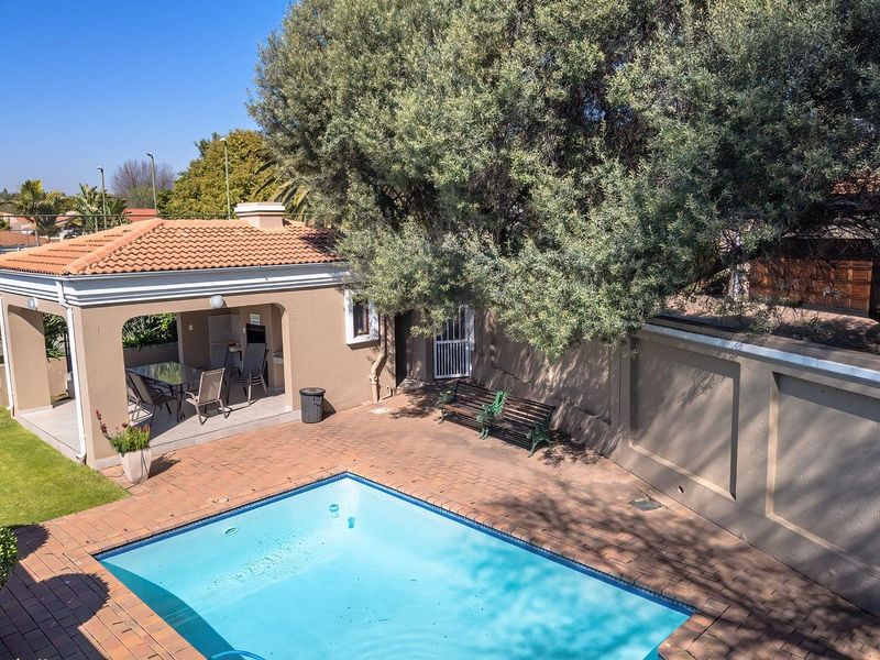 Outdoor entertainment area featuring a swimming pool, brick-paved patio, and a covered patio with a built-in braai, set within a private walled garden.