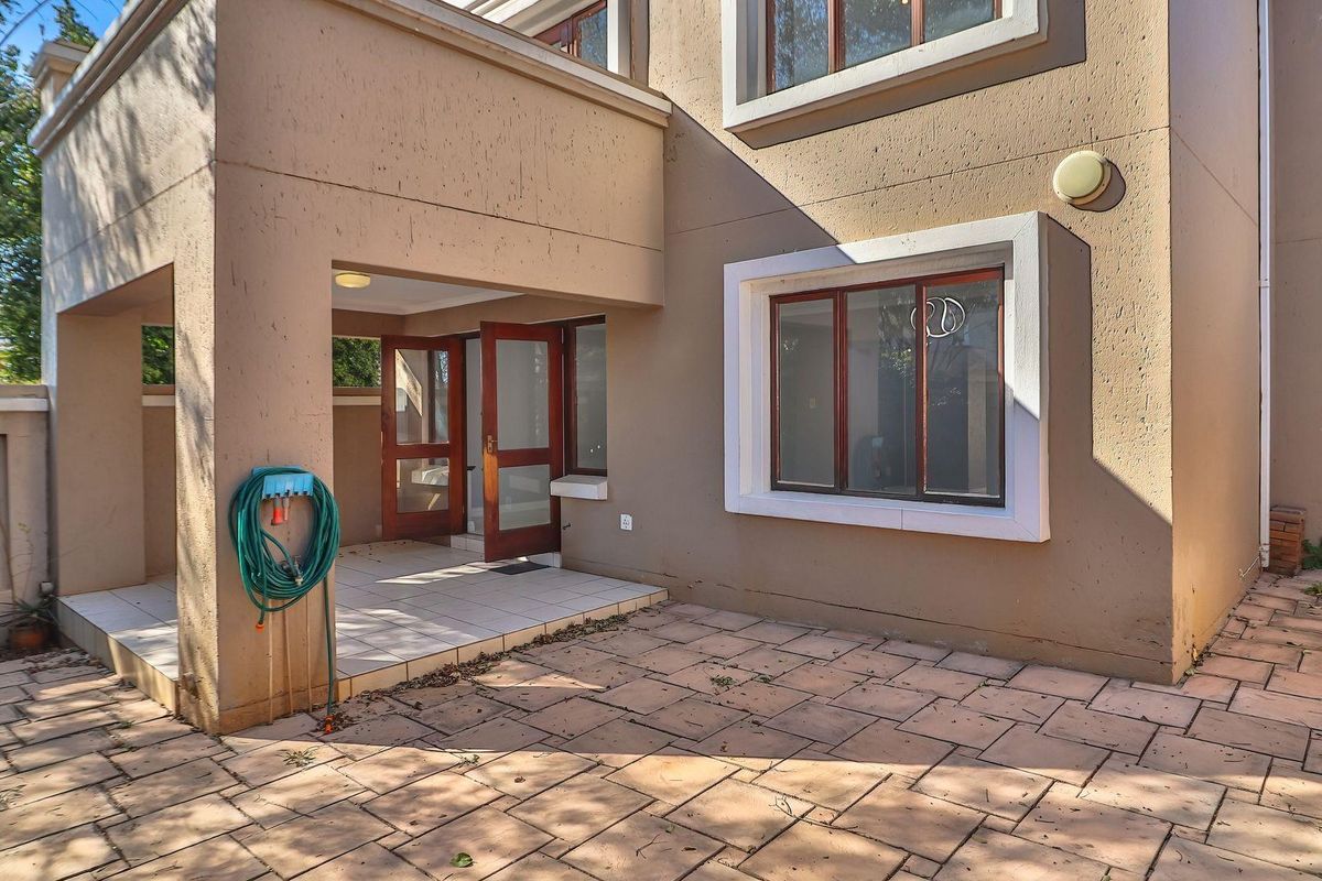 Rear exterior view of the townhouse featuring a covered patio area, paved courtyard, and timber-framed windows and doors.