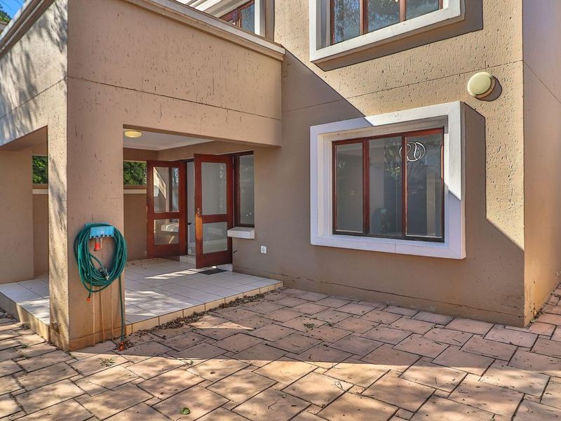 Rear exterior view of the townhouse featuring a covered patio area, paved courtyard, and timber-framed windows and doors.