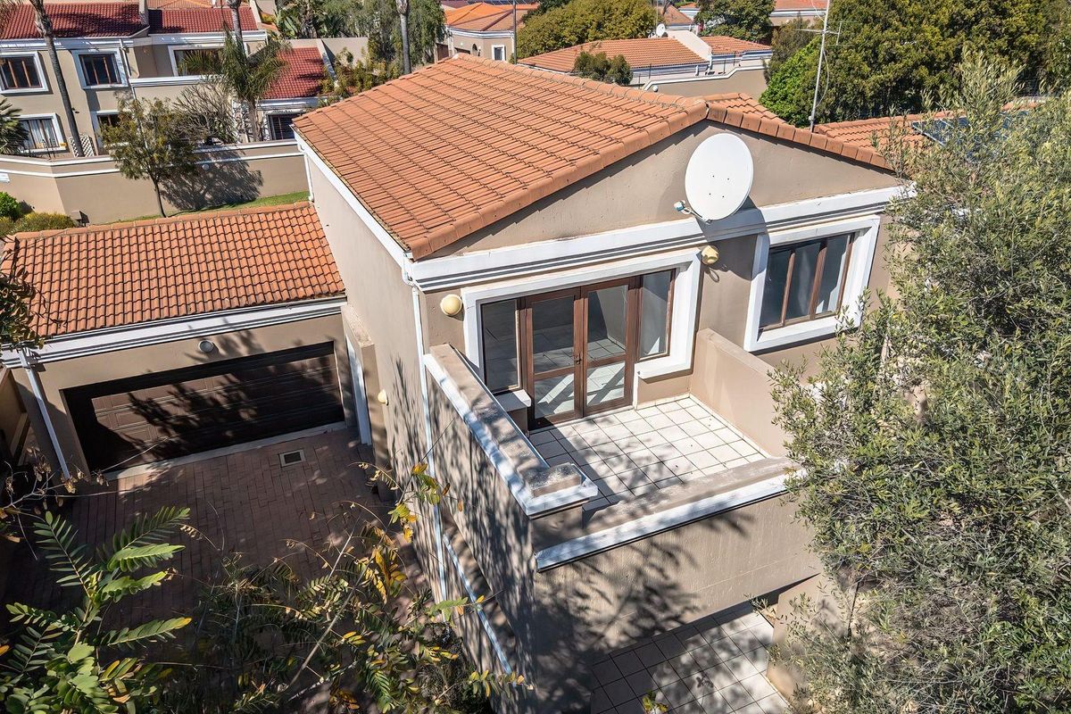 Aerial view of a townhouse featuring a terracotta tiled roof, a paved driveway, a garage, and an upper-level balcony with sliding glass doors.