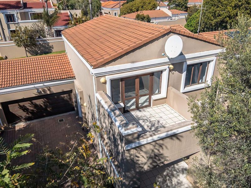 Aerial view of a townhouse featuring a terracotta tiled roof, a paved driveway, a garage, and an upper-level balcony with sliding glass doors.