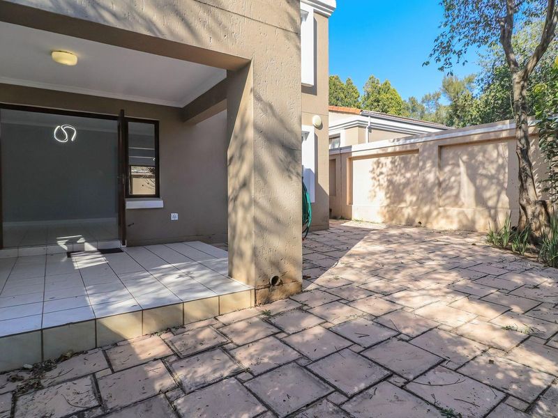 A covered patio area with tiled flooring leading to a paved rear courtyard and boundary wall, offering a private outdoor space.