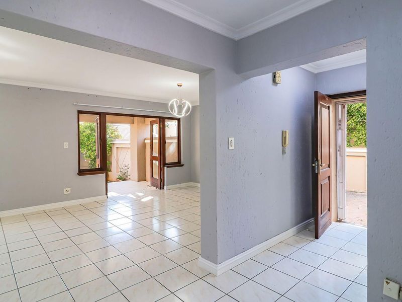An open-plan living area featuring tiled flooring, coved cornicing, and direct access to an outdoor patio through wooden-framed doors.