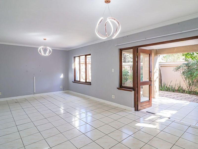 Spacious, light-filled living area featuring neutral walls, tiled flooring, and direct access to an outdoor patio through a timber-framed glass door.
