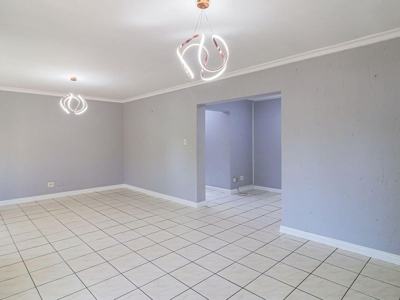 A spacious, empty living area featuring neutral tiled flooring, modern pendant lighting, and cove cornicing, offering a blank canvas for interior design.