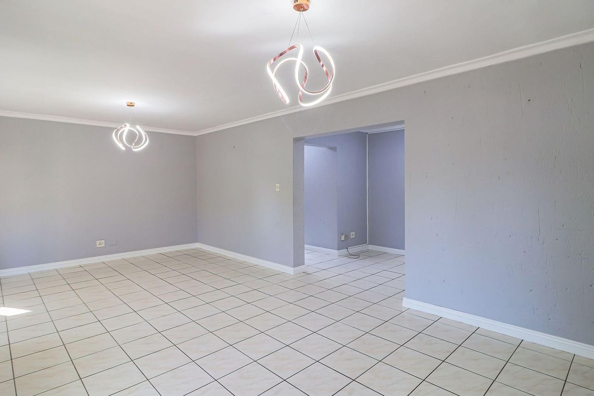 A spacious, empty living area featuring neutral tiled flooring, modern pendant lighting, and cove cornicing, offering a blank canvas for interior design.