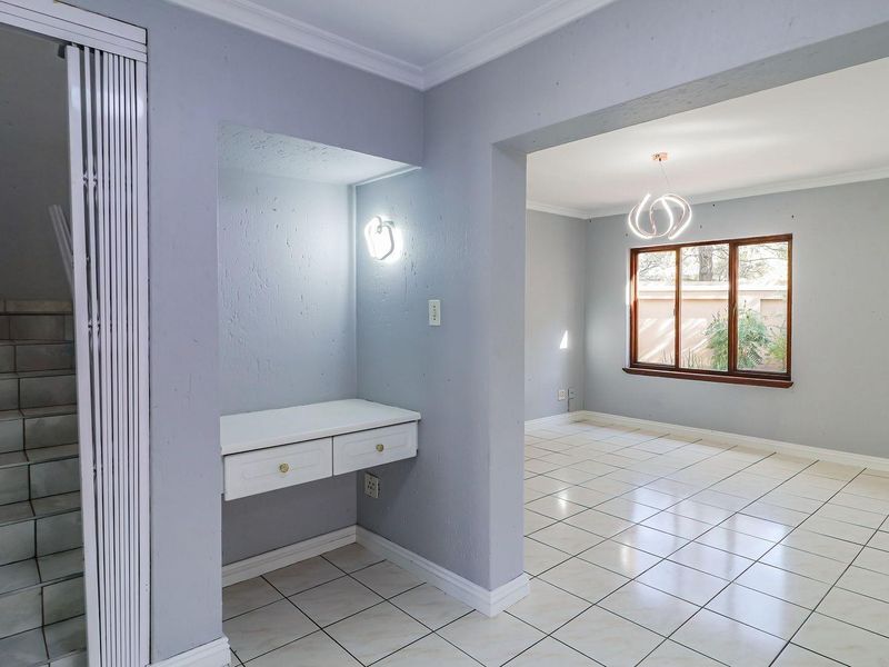 An open-plan living area featuring tiled flooring, a built-in desk nook, and a staircase, offering a bright and versatile space.