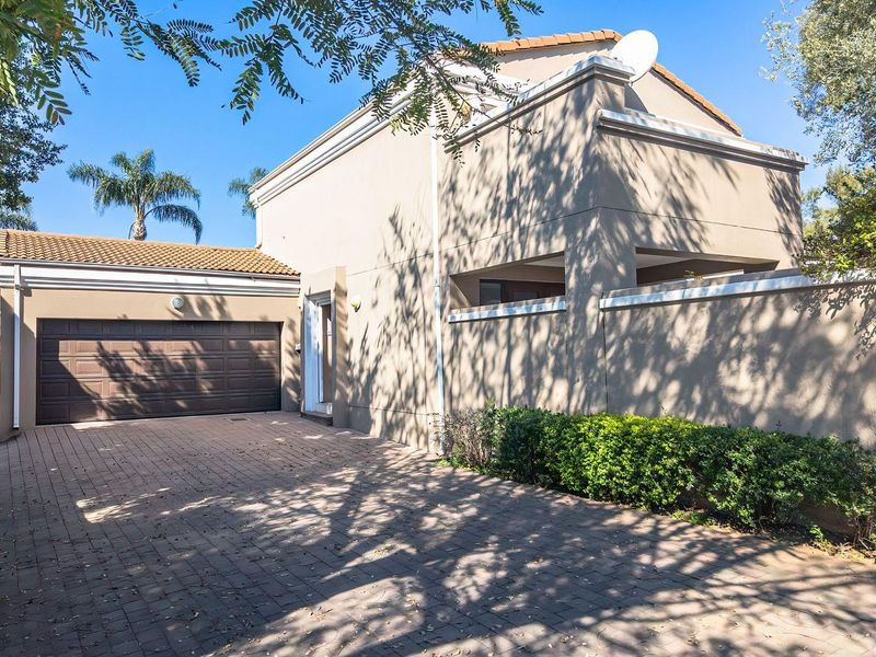 Front exterior view of the townhouse featuring a paved driveway, double garage, and secure boundary walling under a clear sky.