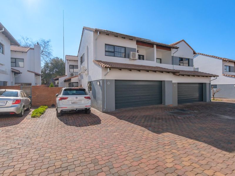 Front exterior view of a townhouse complex featuring a paved driveway, double garage, and multi-level architectural design with tiled roofing.