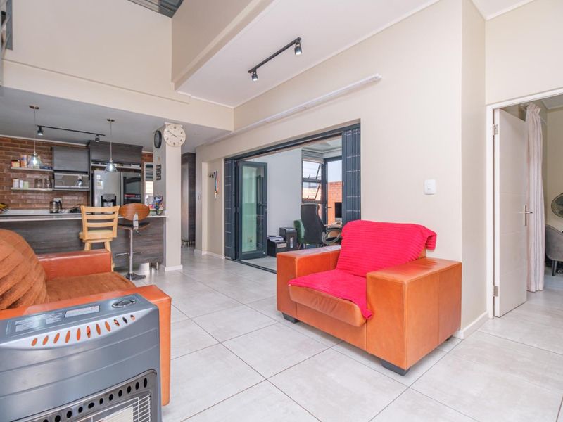 Open-plan living area featuring tiled floors, a modern kitchen with island, exposed brick accents, and stacking doors leading to an outdoor space.