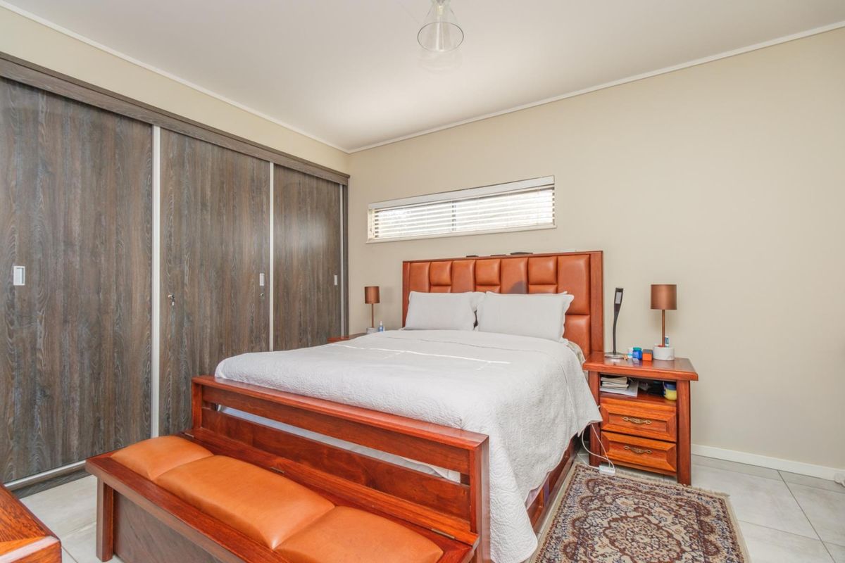 A well-maintained bedroom featuring built-in sliding door wardrobes, tiled flooring, and a horizontal window providing natural light.
