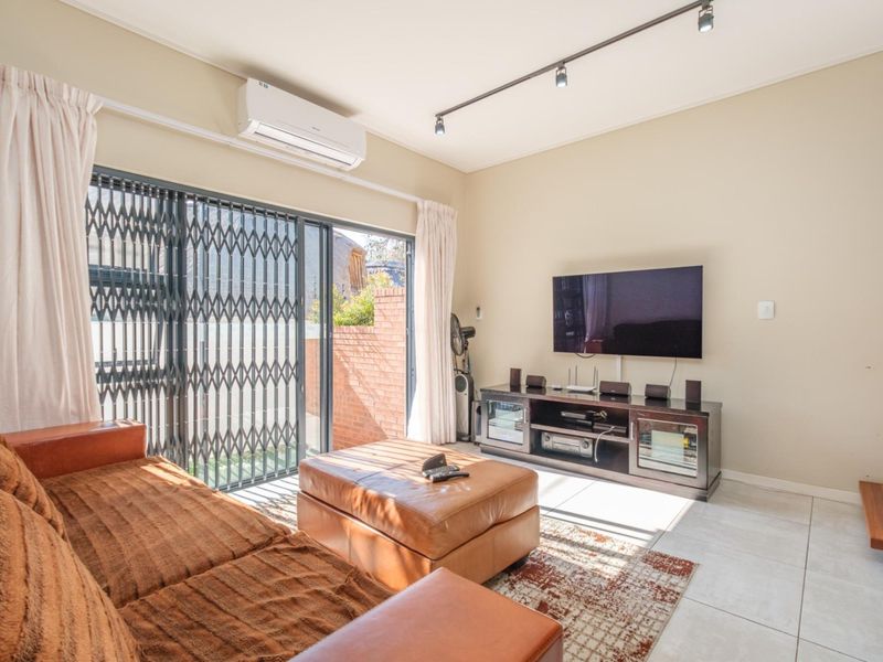 A bright living room featuring tiled flooring, track lighting, a wall-mounted air conditioner, and a sliding glass door leading to an outdoor area.