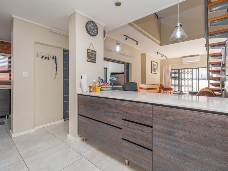 Open-plan living area featuring a modern kitchen island with stone countertops, tiled flooring, and a staircase leading to the upper level.