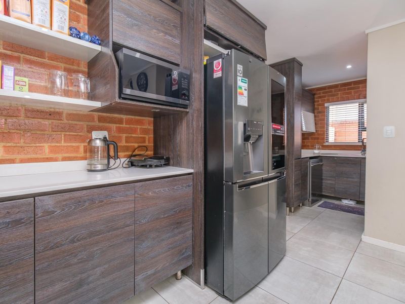 Modern kitchen featuring dark wood cabinetry, exposed brick accents, stone countertops, and integrated appliances with tiled flooring.
