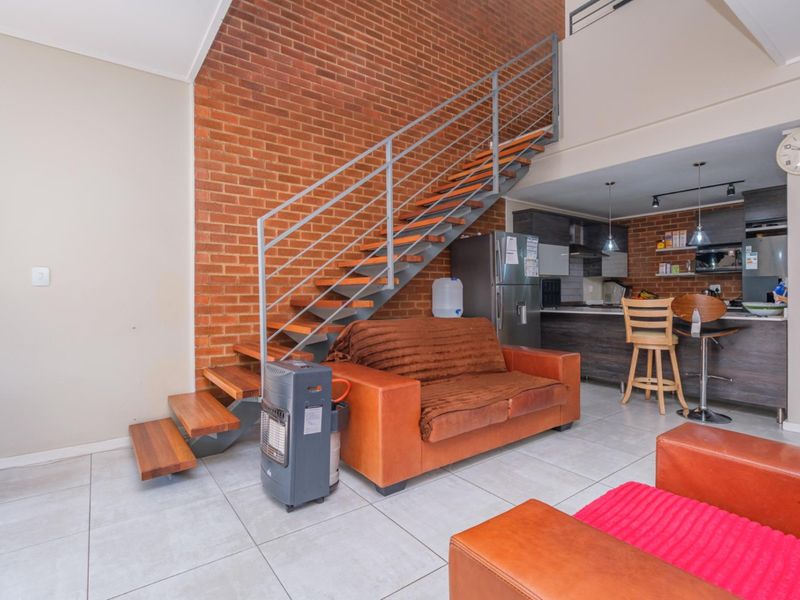 Open-plan living area featuring an exposed brick feature wall, a modern floating staircase, and a functional kitchen with a breakfast bar.