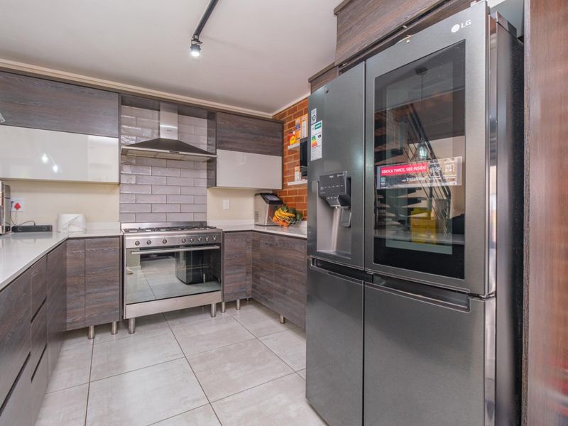 Modern kitchen featuring dark wood-grain cabinetry, stone countertops, subway tile backsplash, exposed brick accents, and high-quality stainless steel appliances.
