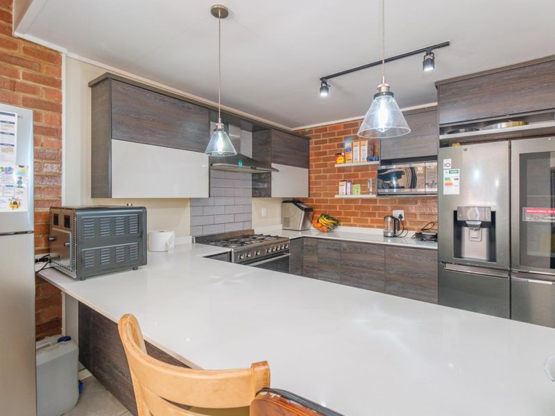 Modern kitchen featuring dark wood cabinetry, white stone countertops, exposed brick walls, and high-quality built-in appliances with stylish pendant and track lighting.