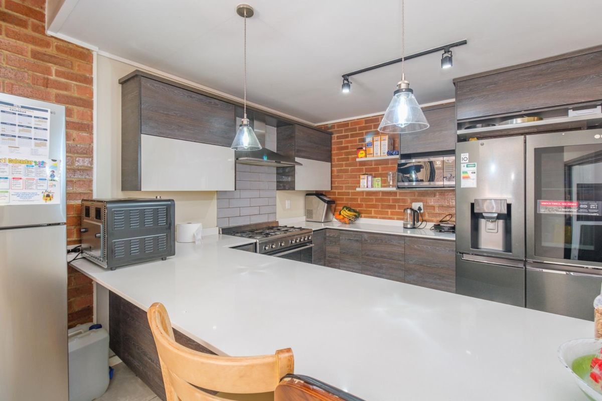 Modern kitchen featuring dark wood cabinetry, white stone countertops, exposed brick walls, and high-quality built-in appliances with stylish pendant and track lighting.