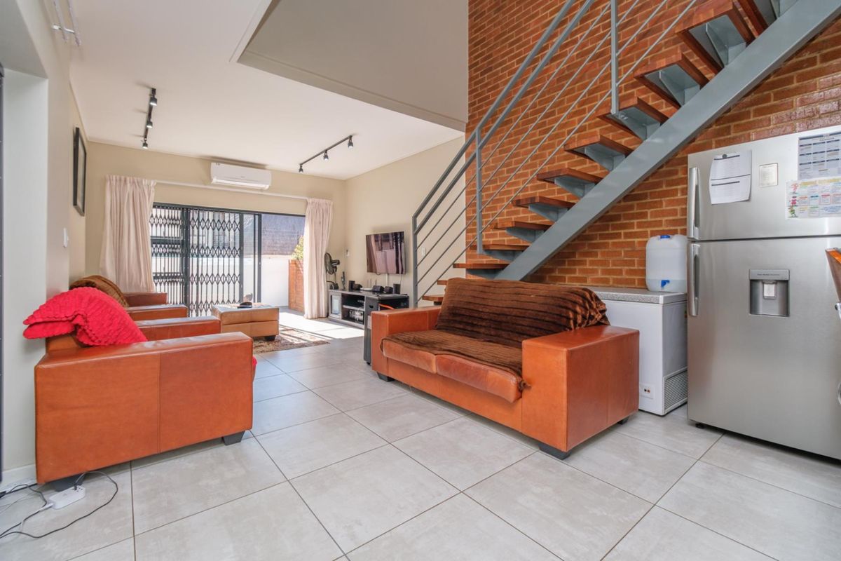 Spacious open-plan living area featuring an exposed brick feature wall, modern metal staircase, tiled flooring, and direct access to an outdoor patio area.