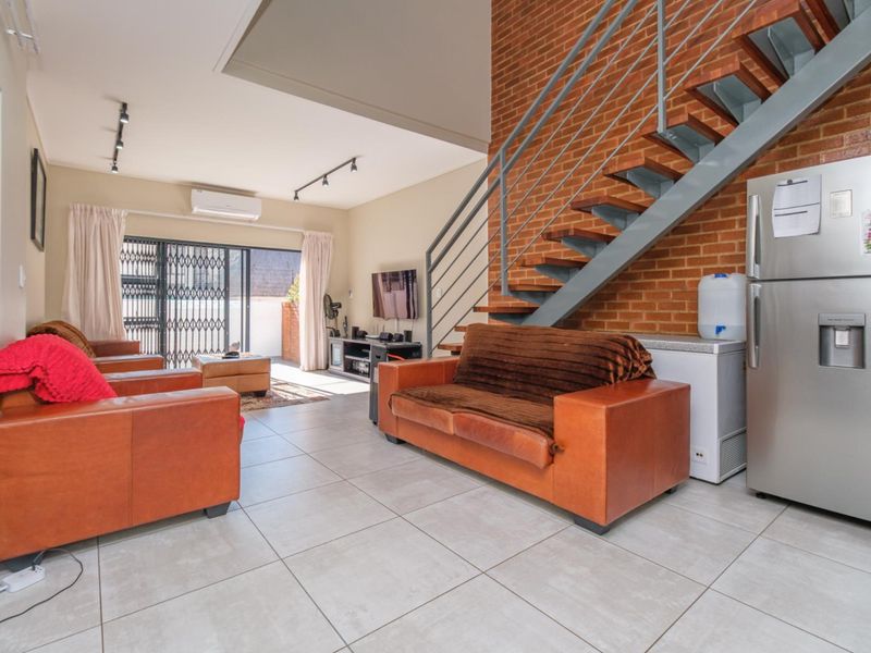 Spacious open-plan living area featuring an exposed brick feature wall, modern metal staircase, tiled flooring, and direct access to an outdoor patio area.
