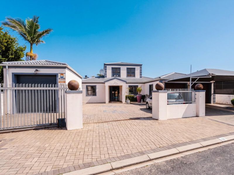 Front view of a residential property featuring a paved driveway, secure metal gate, attached garage, and a covered carport area.
