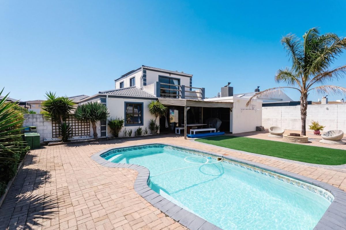 Rear exterior view featuring a swimming pool, paved patio area, artificial lawn, and a covered patio attached to the main dwelling.
