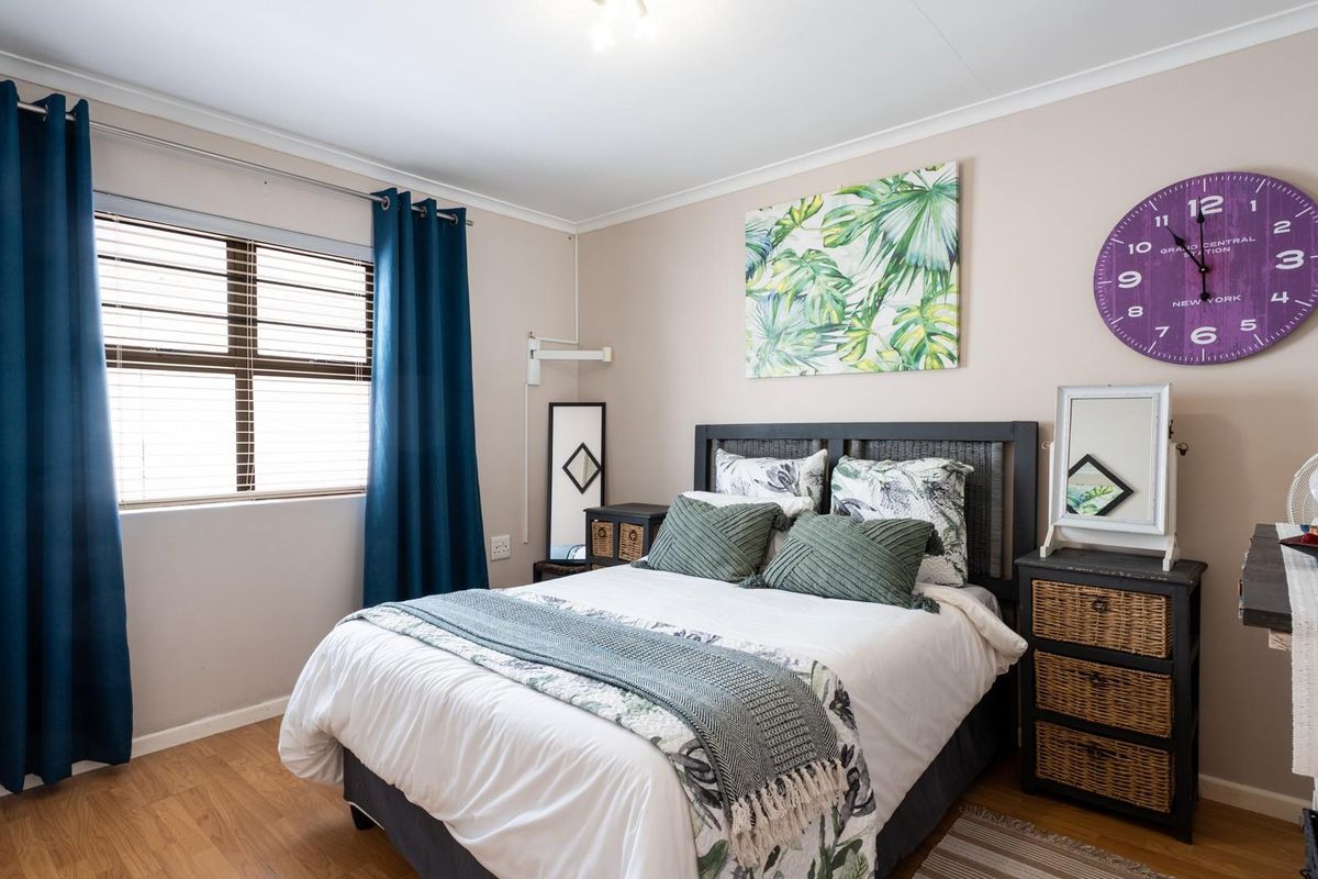 A well-maintained bedroom featuring laminate flooring, neutral wall tones, and a window fitted with blinds and curtain rails.