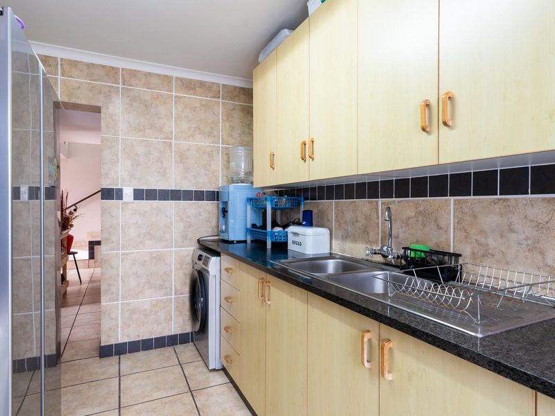 Functional scullery featuring laminate cabinetry, granite countertops, double stainless steel sink, and tiled finishes with integrated laundry plumbing.