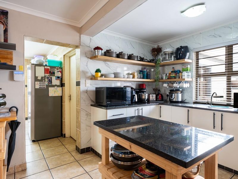 A functional kitchen featuring marble-look wall tiles, granite countertops, floating timber shelving, and ceramic floor tiles, with an adjacent scullery area.