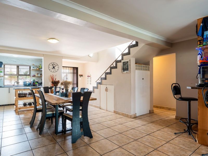 Spacious open-plan living and dining area featuring tiled flooring, a functional kitchen with built-in cabinetry, and a staircase with integrated under-stair storage.