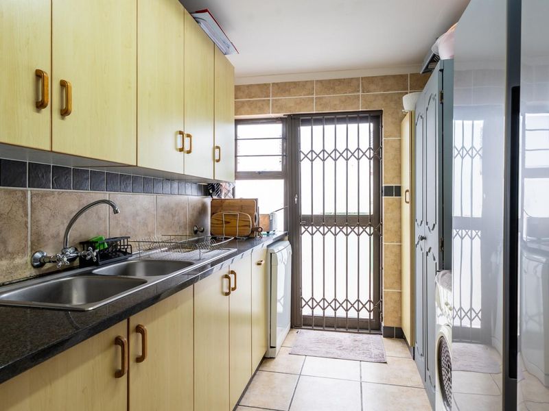 A functional scullery featuring laminate cabinetry, granite countertops, a double basin sink, and direct access to the exterior via a security gate.