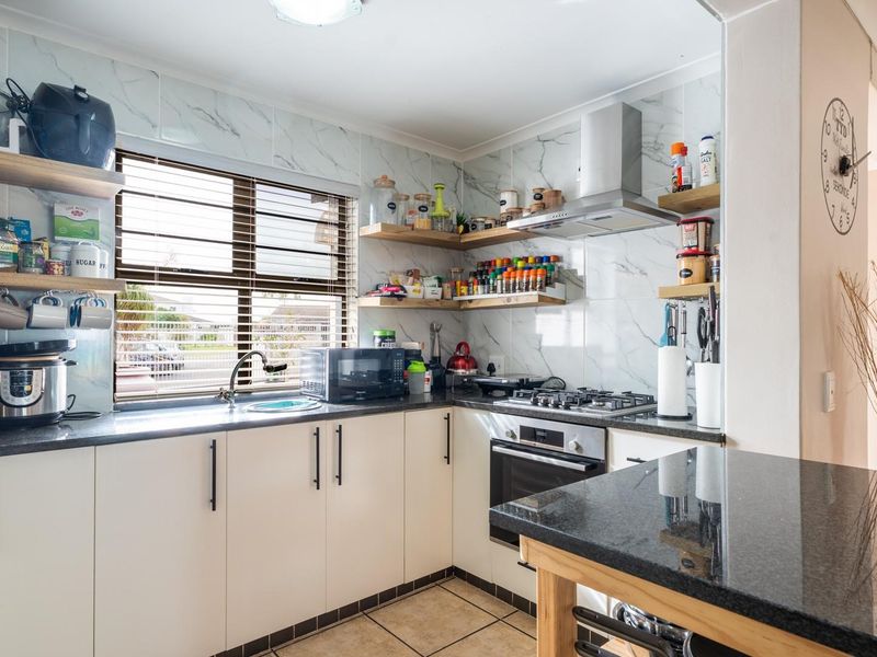 Modern kitchen featuring marble-look wall tiles, granite countertops, built-in oven, gas hob, and floating timber shelving for a clean, functional workspace.