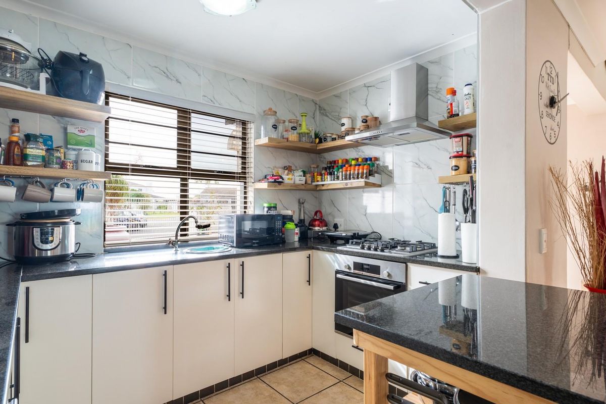 Modern kitchen featuring marble-look wall tiles, granite countertops, built-in oven, gas hob, and floating timber shelving for a clean, functional workspace.