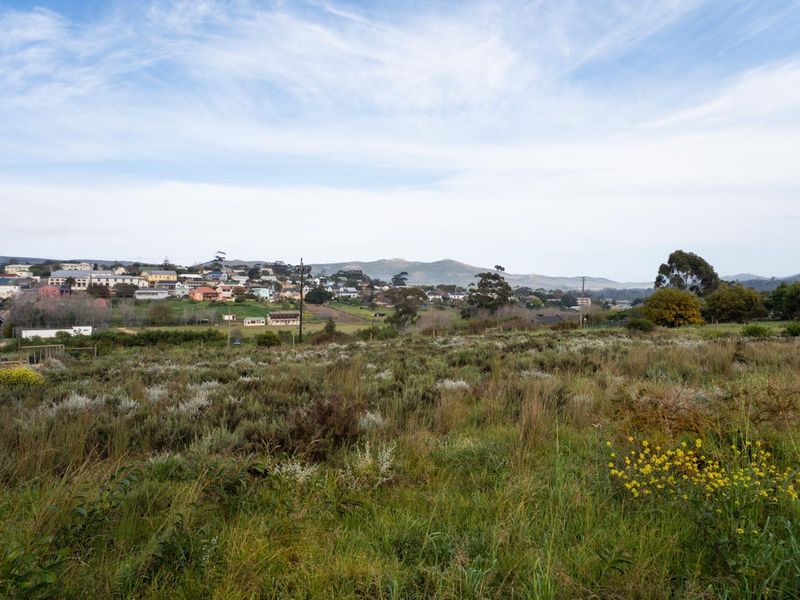 A wide-angle view of a vacant residential plot featuring natural vegetation and distant mountain and town views.