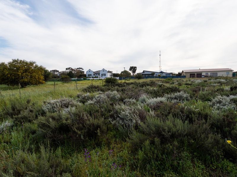 A view of a vacant residential plot featuring natural vegetation and perimeter wire fencing, with neighboring properties visible in the background.