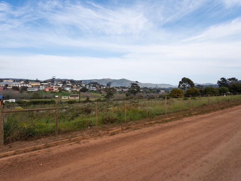 A scenic view of the surrounding landscape and distant residential area, captured from a dirt road bordering the vacant land.