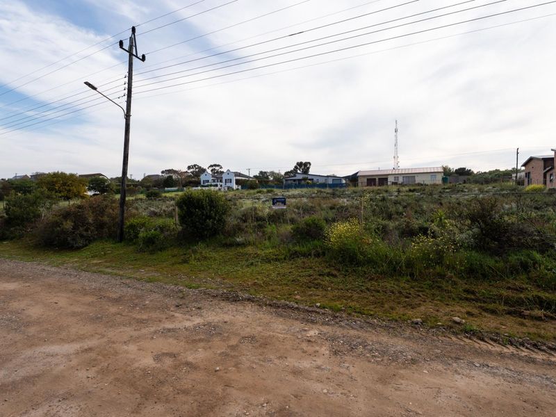 A vacant residential plot featuring natural vegetation, accessible via an unpaved road with existing utility infrastructure nearby.