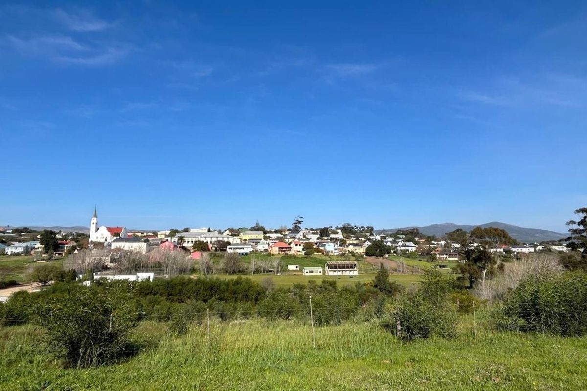 A scenic view overlooking a small town with a church steeple, surrounded by open green fields and rolling hills.