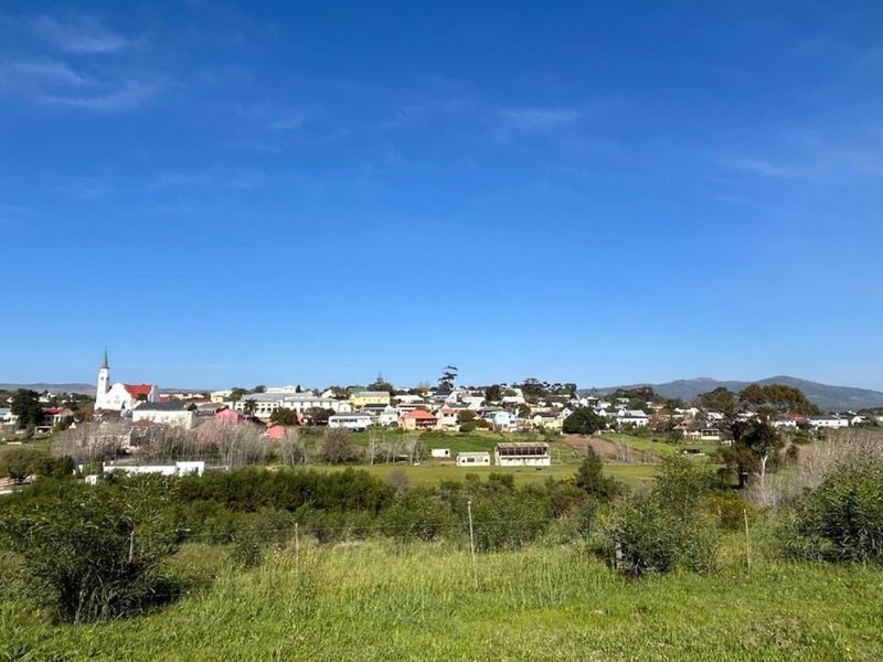 A scenic view overlooking a small town with a church steeple, surrounded by open green fields and rolling hills.