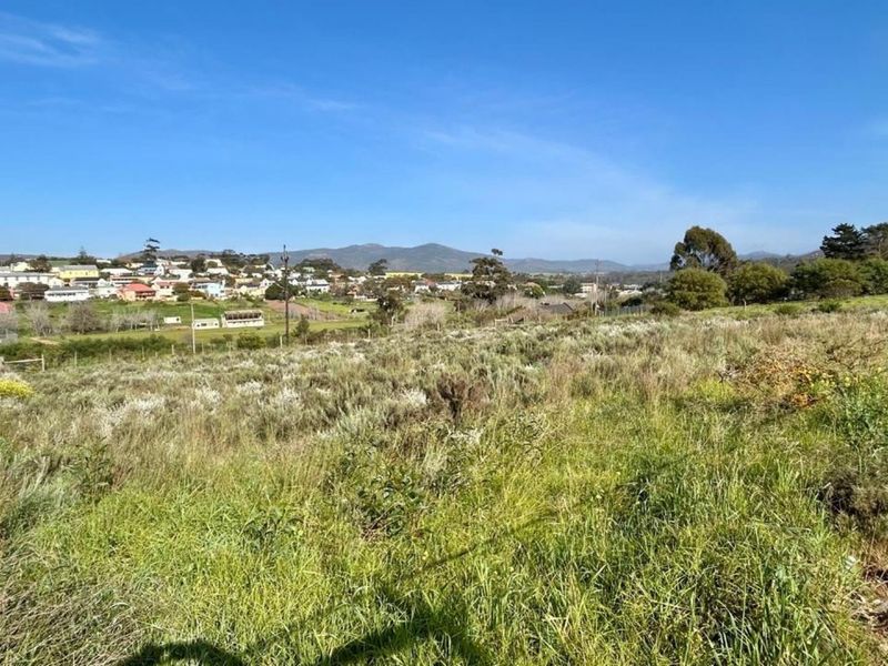 A scenic view overlooking a grassy vacant residential plot with distant mountain and town vistas.