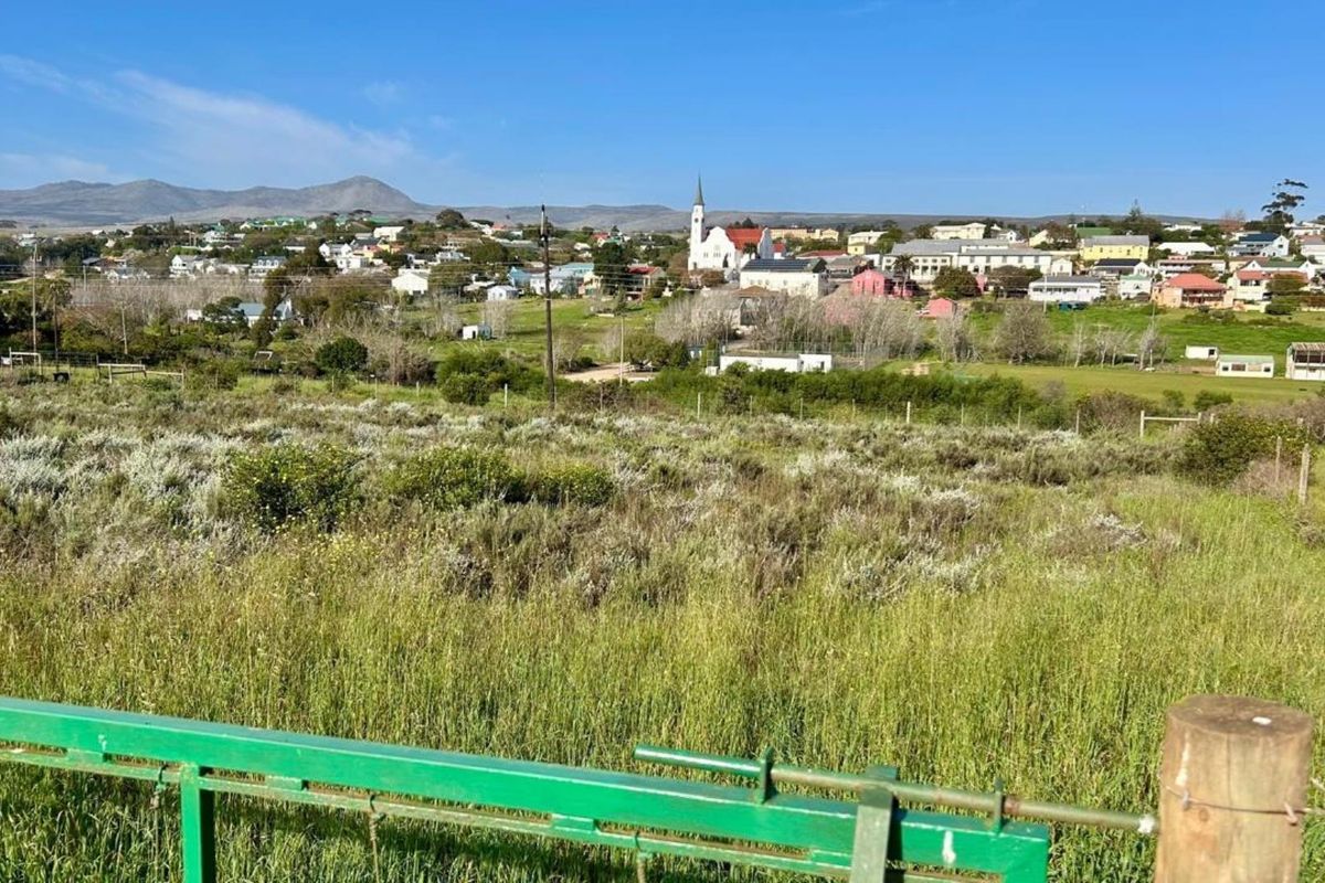 A scenic view overlooking a residential town with a church steeple, featuring a foreground of undeveloped land with perimeter fencing.