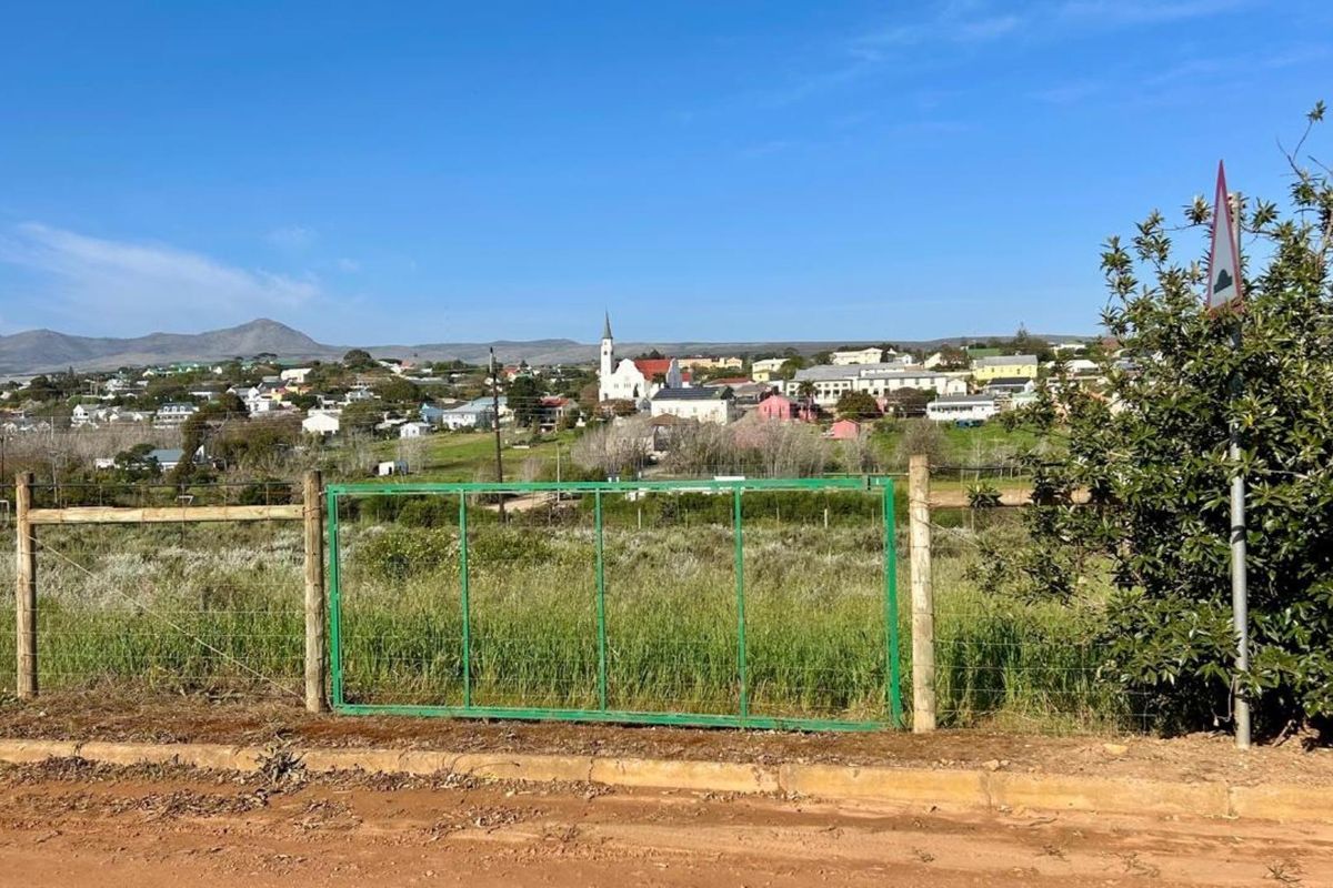 A view of the surrounding town and landscape from the vacant residential plot, featuring a wire fence and metal gate boundary.