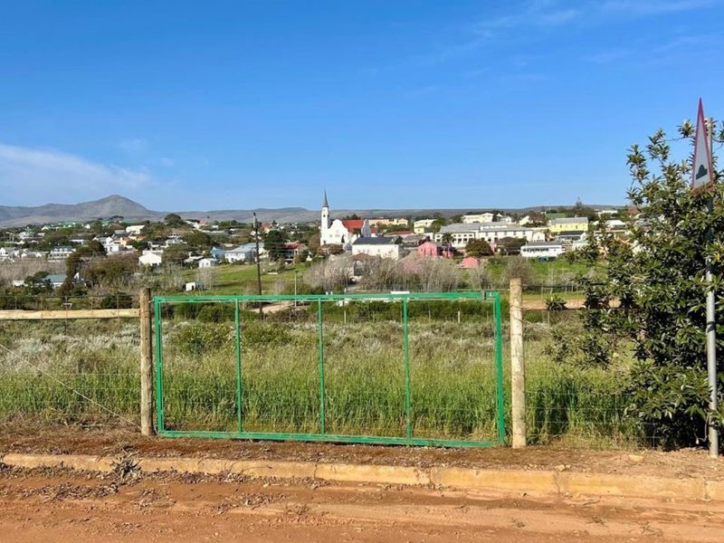A view of the surrounding town and landscape from the vacant residential plot, featuring a wire fence and metal gate boundary.
