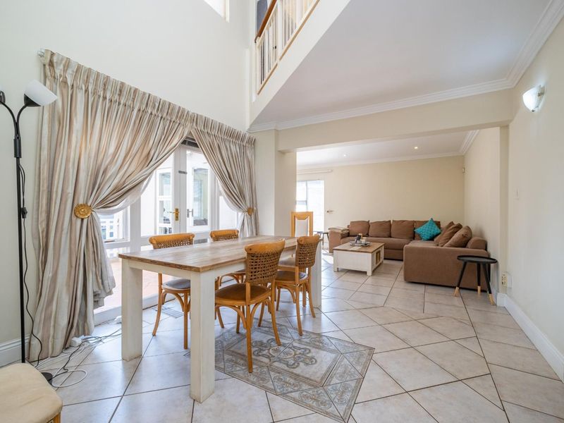 Spacious open-plan living and dining area featuring double volume ceilings, tiled flooring, and direct access to the patio through french doors.